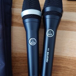 Dvě černé dynamické mikrofony značky AKG. Levý mikrofon má stříbrný prstenec pod mřížkou a nápis D5 v dolní části těla. Pravý mikrofon má nápisy PERC…