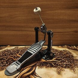 Fotografie znázorňuje basový pedál v černé a stříbrné barvě. Na stupni je viditelný nápis YAMAHA. Pedál má kovové provedení s gumovou protiskluzovou…