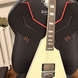 Bílá elektrická kytara s ostrým, asymetrickým tvaru těla a špičatou hlavou. Na hmatníku jsou vidět obdélníkové vložky a na těle je jeden humbucker s…