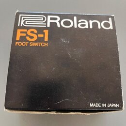 Černá kartonová krabice s bílým logem Roland. Pod ním je oranžový nápis FS-1 a bílý text FOOT SWITCH. V pravém dolním rohu je bílý nápis MADE IN JAPA…