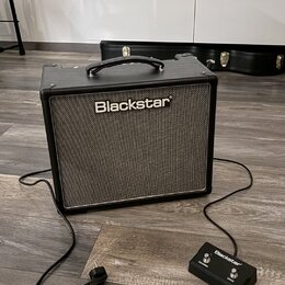 Černý kytarový kombo zesilovač s šedým textilním krytem reproduktoru a nápisem Blackstar. K zesilovači je připojen černý nožní spínač s logem Blackst…