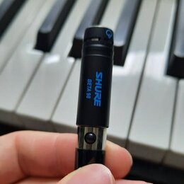 Černý cylindrický mikrofon s modrým nápisem SHURE BETA 98. Na horní části je vidět malý modrý symbol. Povrch mikrofonu je matný a v dobrém stavu, spo…