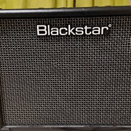 Černý kytarový kombo zesilovač s texturovaným povrchem a mřížkou reproduktoru. V horní části je bílý nápis Blackstar. Nástroj vykazuje mírné opotřebe…