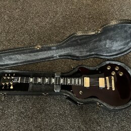 Tmavě hnědá elektrická kytara v otevřeném černém tvrdém pouzdře. Na hlavě nástroje je bílé logo Gibson. Kytara má dva humbuckery s krémovými kryty, z…