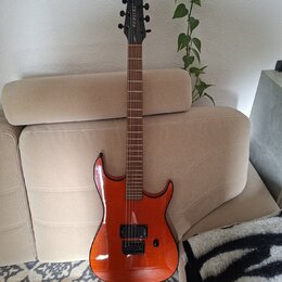 Elektrická kytara s oranžovým lakovaným tělem a hnědým hnedým hmatníkem. Na hlavě je vidět bílý nápis "Ibanez". Kytara má dva humbuckery, jeden ovlád…