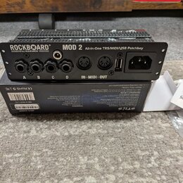 Černý patchbay s nápisem ROCKBOARD by WARWICK MOD 2 All-in-One TRS/MIDI/USB Patchbay. Zařízení obsahuje čtyři jack konektory označené písmeny A, B, C…