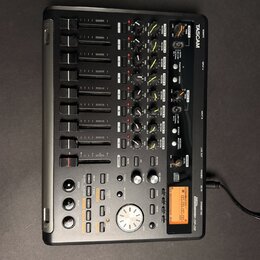Černý digitální multitrackový nahrávací studiový mixér značky TASCAM, model DP-02. Zařízení obsahuje několik faderů, otočných knoflíků a ovládacích t…