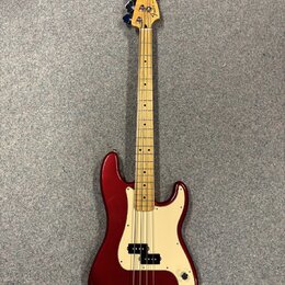 Třístrunná elektrická basová kytara s vínovým lakovaným tělem a krčkem z jasného dřeva. Na hlavě je viditelné logo Fender. Bílý pickguard obsahuje dv…
