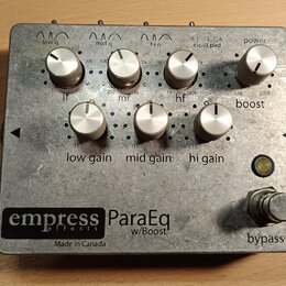 Kytarový efekt pedál v kovovém šasi stříbrné barvy. Na spodní části je černý štítek s nápisy „empress effects ParaEq w/Boost“ a pod ním text „Made in…