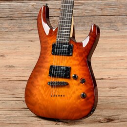 Elektrická kytara s tělem v oranžovém probarvování s viditnou strukturou dřeva. Nástroj má dva černé humbuckery, tři černé ovládací knofíky a černý m…