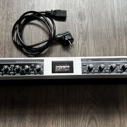 Stříbrné rackové zařízení s černým předním panelem a nápisem ULTRAGAIN PRO. Na pravé straně je logo a značka behringer oraz vypínač POWER. Přístroj o…