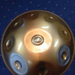 Kovový perkusní nástroj typu steel tongue drum v bronzové barvě. Nástroj má kulovitý tvar s několika vlisnými otvory rozmístěnými po povrchu. Povrch…