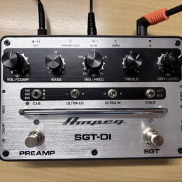 Stříbrný kytarový preamp s nápisem Ampeg a modelem SGT-DI. Zařízení má pět černých otočných ováčků s popisky VOL / COMP, BASS, MID / FREQ, TREBLE a G…