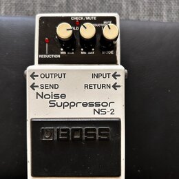 Kytarový pedál značky BOSS, model Noise Suppressor NS-2. Zařízení má bílé tělo s černým ovládacím panelem a černým spínacím pedálem. Na horní části j…