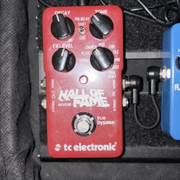 Červený kytarový efekt s nápisy HALL OF FAME REVERB a tc electronic. Na horní straně jsou čtyři černé ovládací knoflíky s popisky DECAY, PRE-DELAY, T…