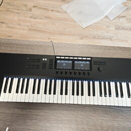 Černý MIDI kontrolér s klávesnicí. Na levé straně je bílý nápis KOMPLETE s logem vedle. Horní panel obsahuje několik sad tlačítek, dva displeje a jed…