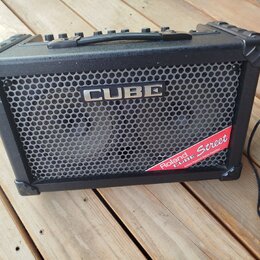Černý kytarový kombo zesilovač s kovovou mřížkou a plastovými rohovými chrániči. Na mřížce je nápis CUBE a v pravém dolním rohu červená nálepka s tex…