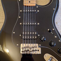 Černá elektrická kytara s jasným javorovým hmatníkem a černým pickguardem. Nástroj má tři snímače, jeden z nich je v pozici bridge humbucker. Na ovlá…