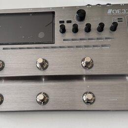 Stříbrný efektový procesor s kovovým povrchem a displejem. Na horním panelu je nápis GE3CC Amp modeling & Multi effects, dále označení EXP1, EXP2, XL…