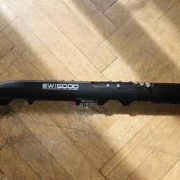Černý elektronický dechový nástroj s nápisy EWIS5000 WIRELESS ELECTRONIC WIND INSTRUMENT a AKAI PROFESSIONAL. Nástroj leží na dřevěné podlaze. Povrch…