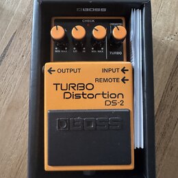 Kytarový efekt v oranžovém provedení s černým pedálem, umístěný v černé krabici značky BOSS. Na přístroji jsou nápisy TURBO Distortion DS-2, OUTPUT,…
