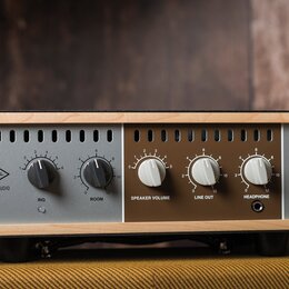 Audio zařízení v dřevěném rámu s šedým a hnědým předním panelem. Na levé straně je logo UA a nápis UNIVERSAL AUDIO, vedle něj knoflíky s popisky RIG…