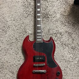 Červená elektrická kytara s černým pickguardem a hnedým hmatníkem. Na hlavě je viditelné logo Epiphone. Tělo vykazuje drobné známky opotřebení a povr…