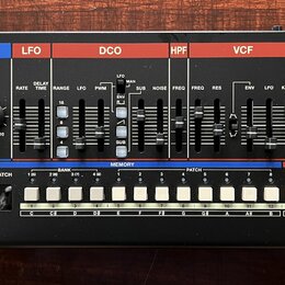 Černý syntetizátor s ovládacími prvky v horní části rozdělenými do barevných sekcí: KEYBOARD, ARPEGGIO, LFO, DCO, HPF, VCF, VCA a ENV. Na přední stra…