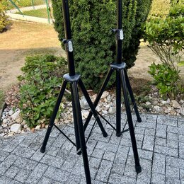 Dvě černé stativy na mikrofony z kovových trubek s trojnožkou. Každý stativ má v horní části bílý plastový knoflík pro utahování. Povrch je černý a v…