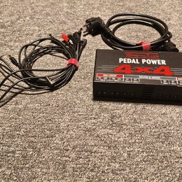 Černý napájecí adaptér Voodoo Lab PEDAL POWER 4x4 s nápisy HIGH CURRENT a ISOLATED DC OUTPUTS. K zařízení patří napájecí kabel do zásuvky a sada čern…