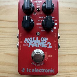 Červený kytarový efekt s nápisem HALL OF FAME 2 a logem tc electronic. Na horní části jsou čtyři černé ovládací knoflíky a nápisy PRE-DELAY (SHORT, L…