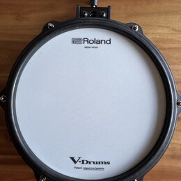 Elektronický buben s bílým pleteným povrchem a černým obručováním. Na horní části je nápis Roland MESH HEAD a v dolní části V-Drums s doplňkem Patent…