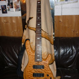 Elektrická basová kytara s přírodním dřevěným povrchem a hnědým hmatníkem. Nástroj má dva černý humbuckery, čtyři ovládací knoflíky a černý popruh. N…