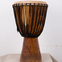 Djembe s dřevěným korpusem v přirozené hnědé barvě. Horní část je obvolta opletena černými provazy, které drží napnutou koženou membránu. Spodní část…