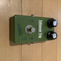 Zelený efekt pedál s kovovým šasi a dvěma černými ovládacími knoflíky s kovovými vršky. Na horní straně je nápis Enhancer Trip a Sonic Filter, vlevo…