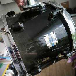 Černý buben s chromovanými obručmi a ladicími šrouby. Na korpusu je viditelný bílo-modrý štítek s nápisy YAMAHA, Stage Custom a MADE IN JAPAN. Povrch…