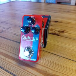 Červený kytarový efekt s nápisem Subnup a pod ním menším textem BASS OCTAVER. Na horní straně jsou tři černé otočné oválné knoflíky s popisky DRY, SU…