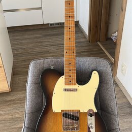 Elektrická kytara s tónem sunburst, krčkem a hmatníkem z přírodního dřeva. Na hlavě je viditelné logo Fender. Kytara má krémový pickguard a chromovan…