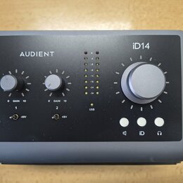 Šedý audio rozhraní s nápisy AUDIENT a iD14. Zařízení má velký ovládací knoflík, dva menší knoflíky s označením GAIN 0 10 u kanálů 1 a 2, dva přepína…