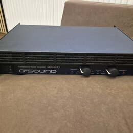 Černý výkonový zesilovač v rackovém provedení s úchyty po stranách. Na předním panelu je nápis Professional Power Amplifier QSA 600 a logo Q SOUND. Z…