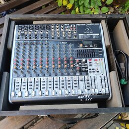 Stříbrný mixážní pult značky behringer s nápisem XENYX QX1832USB umístěný v černé dřevěné bedně. Zařízení obsahuje numerous červené a šedé otočné kno…