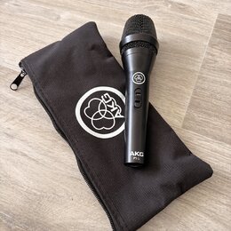 Černý dynamický mikrofon s mřížkou, na těle kterého je nápis AKG P5 S a logo výrobce. Vedle mikrofonu je černý látkový přepravní vak s bílým logem AK…