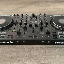 Černý DJ kontrolér s dvěma jog-koly a centrálním mixážním sekcí. Na přístroji jsou viditelné nápisy Numark, serato a modelové označení NS4 FX. V horn…