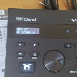 Černý elektronický modul s nápisy Roland a V-Drums. Na displeji je text DRUM KIT 25 Percussion a v pravém dolním rohu nápis DRUM SOUND MODULE TD-07.…