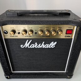Kytarový kombo zesilovač značky Marshall, model DSL1. Má černé provedení s texturovaným povrchem a zlatý ovládací panel s několika otočnými knoflíky.…