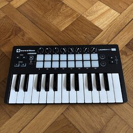 Černý kompaktní MIDI kontrolér s klávesnicí a bílými padovými tlačítky. Na zařízení jsou nápisy novation, LAUNCHKEY MINI a IN CONTROL. Povrch je v do…