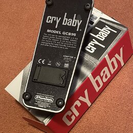 Fotografie zachycuje spodní stranu efekt pedálu v černé barvě s kovovým tělem. Na povrchu jsou nápisy „cry baby“, „MODEL GCB95“ a logo „Dunlop“. Je z…