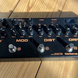 Černý kytarový efekt pedál s nápisy DELAY, MOD, DIST a DRIVE. Na spodní pravé straně je uveden název modelu Cerberus a značka NUX, dále nápisy TRUE B…