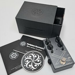 Kytarový efekt pedál stříbrné barvy s černými ovládacími knoflíky a nápisy MICROTUBES X, Darkglass Electronics - MADE IN FINLAND. Vedle pedálu je čer…