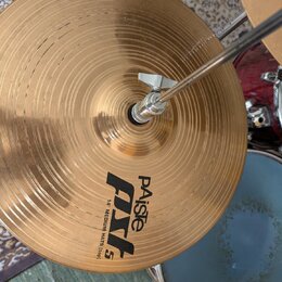 Zlatý kovový činel s koncentrickými drážkami, který je upevněn na stojanu pomocí motýlkového šroubu. Na povrchu je černý nápis „Paiste PSL 5“ a pod n…